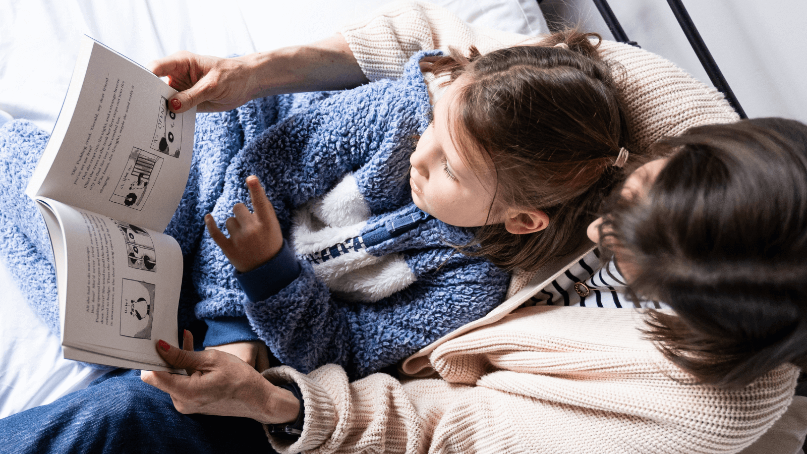 A girl sitting on a mother's lap looking at a chapter book together