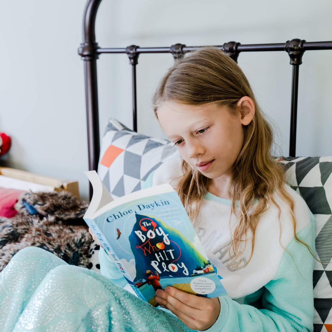 Girl wearing pyjamas sat on a bed reading a chapter book