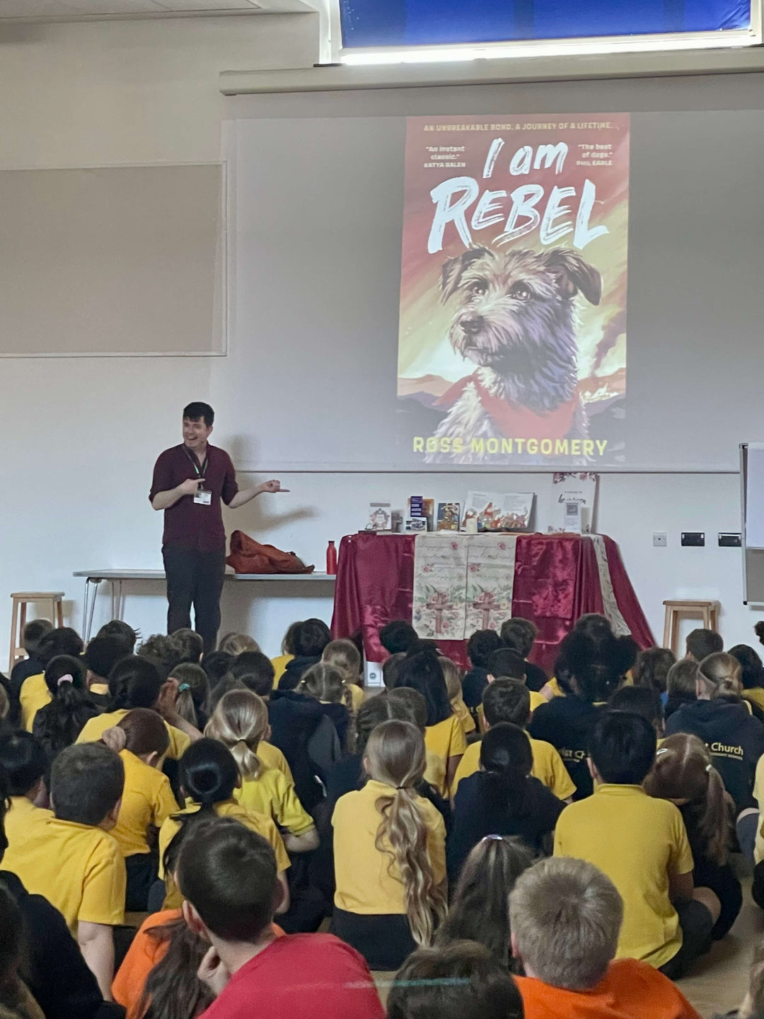 Ross Montgomery leading a school event, cover of I am Rebel on the screen.