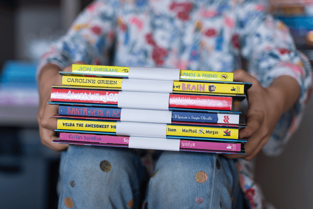 Child holding a bundle of chapter books and activity packs on their lap