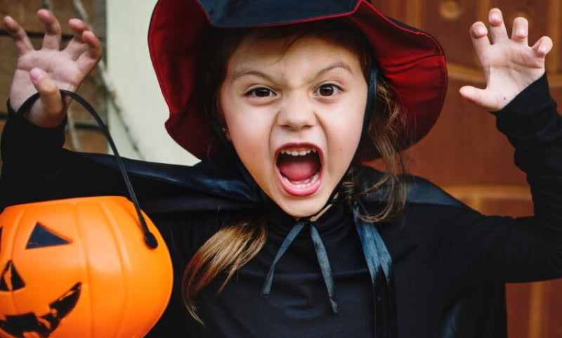 Girl in witch costume holding Halloween pumpkin basket