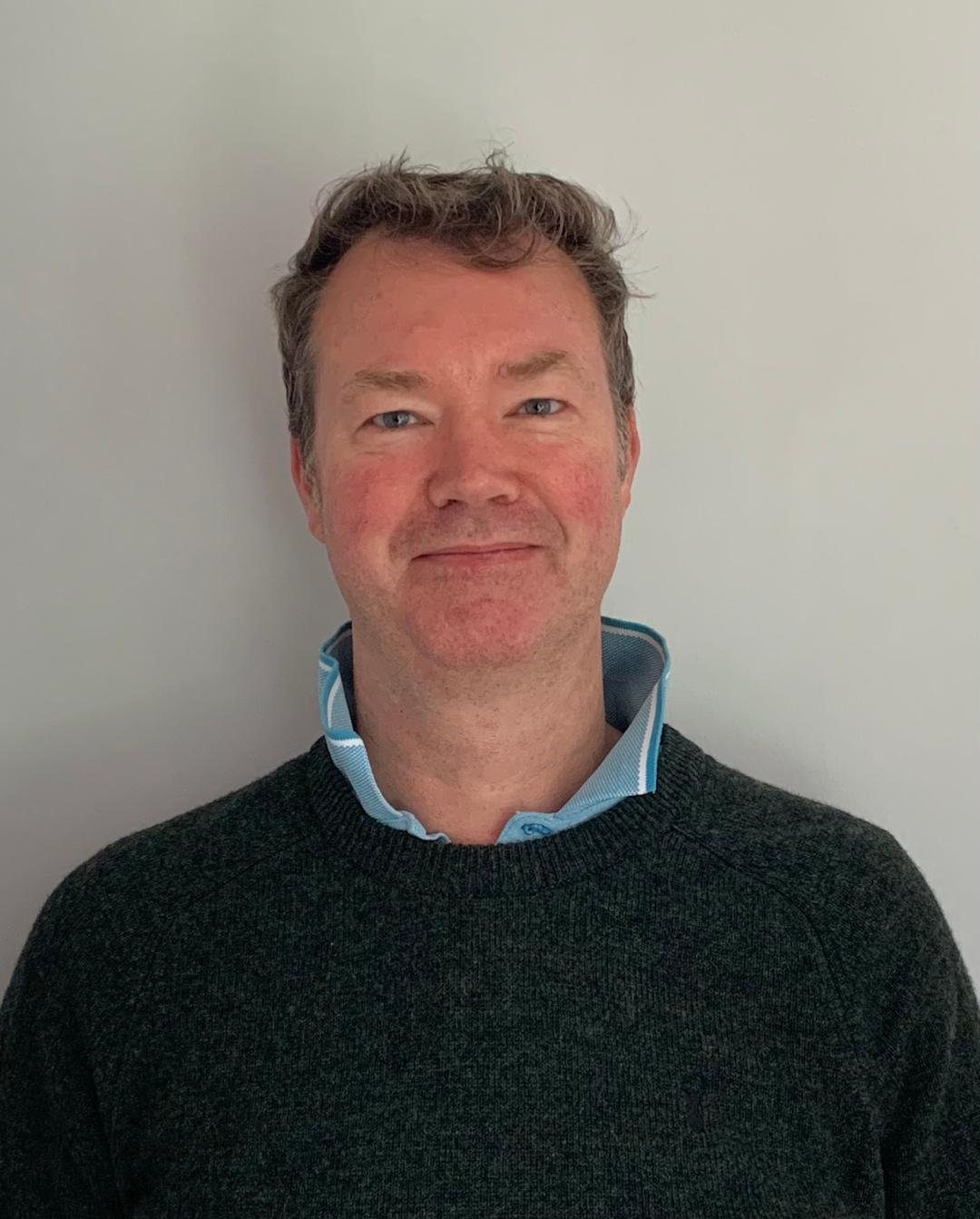 Author Simon Fox wearing a dark sweater over a light shirt against a plain background