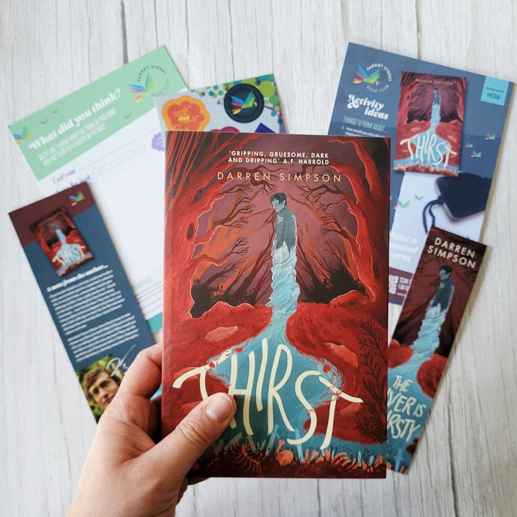 Book titled 'Thirst' by Darren Simpson held by a hand with promotional materials on a light wooden surface.