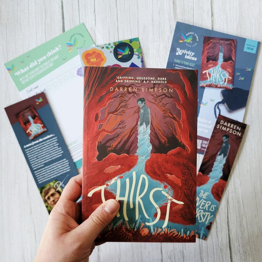Book titled 'Thirst' by Darren Simpson held by a hand with promotional materials on a light wooden surface.