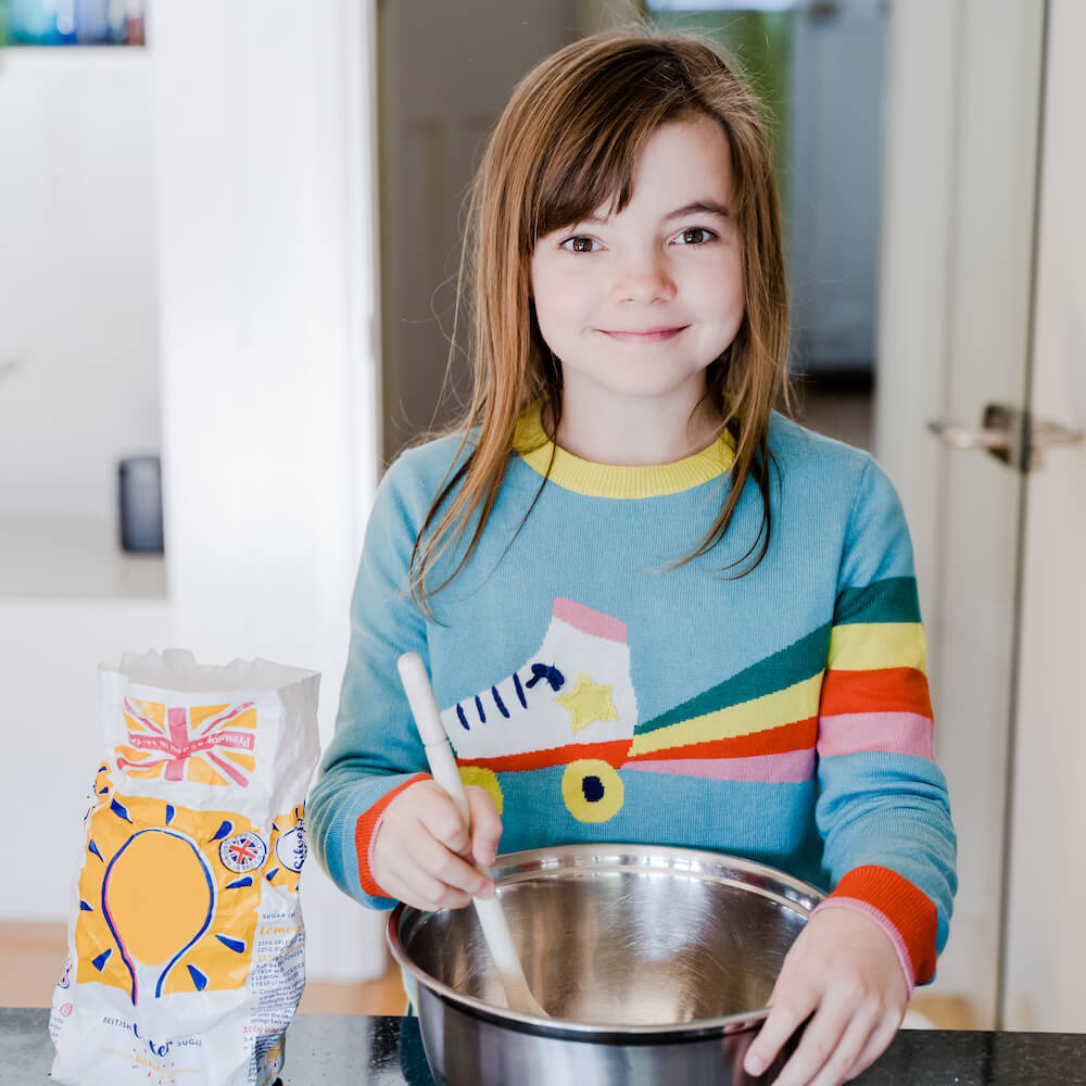 A girl using a spoon and mixing bowl, as part of a cooking activity suggested in a Parrot Street Book Club pack.
