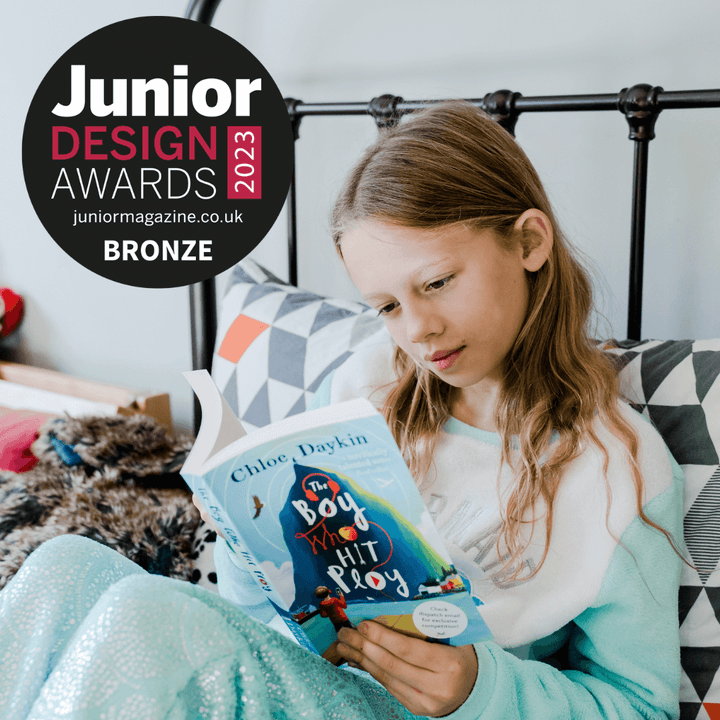 A girl sitting on a bed reading a chapter book. Logo over the top denotes Junior Design Awards 2023 Bronze winner