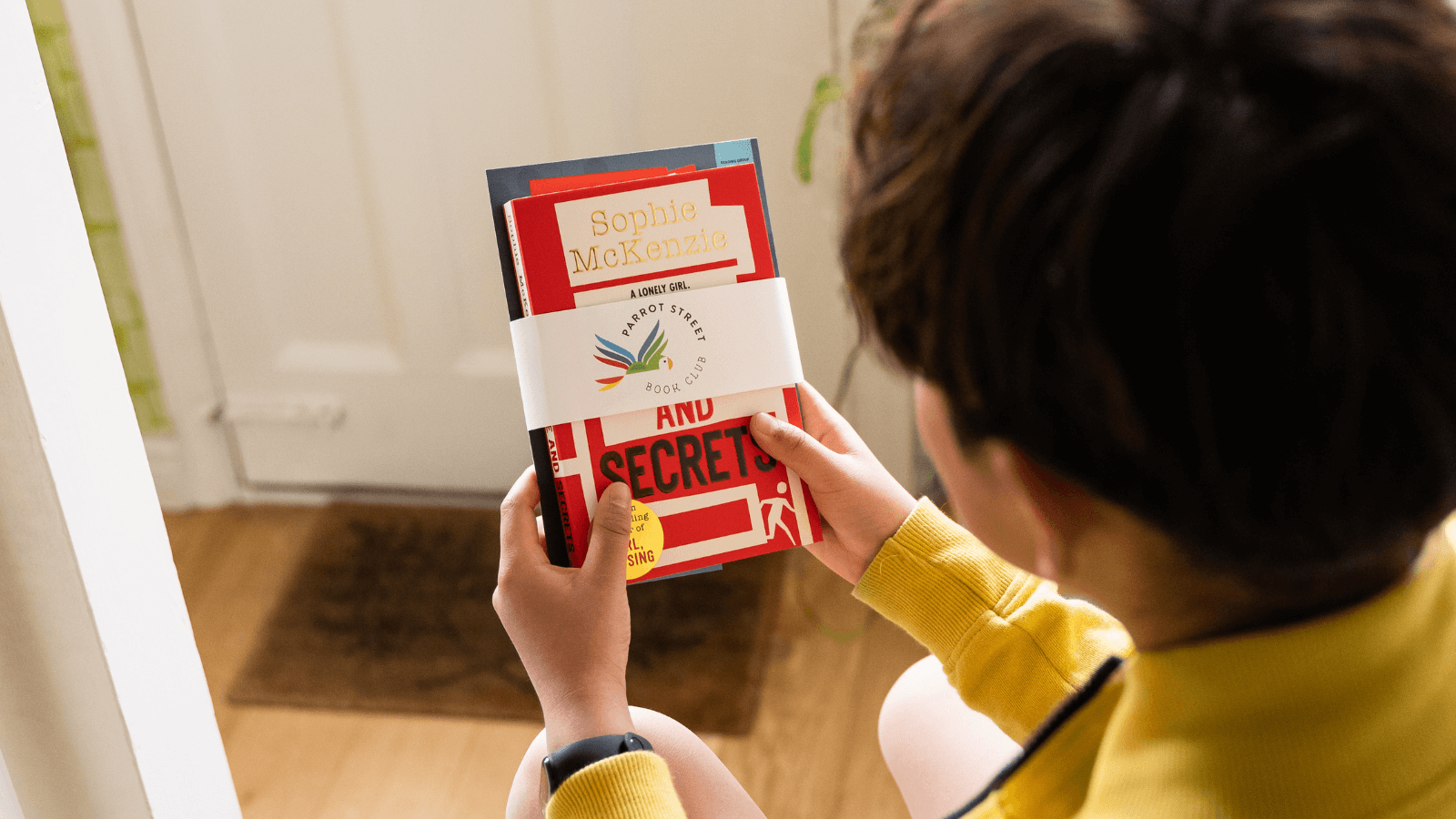 A child holding a wrapped Parrot Street Book Club chapter book and activity pack bundle