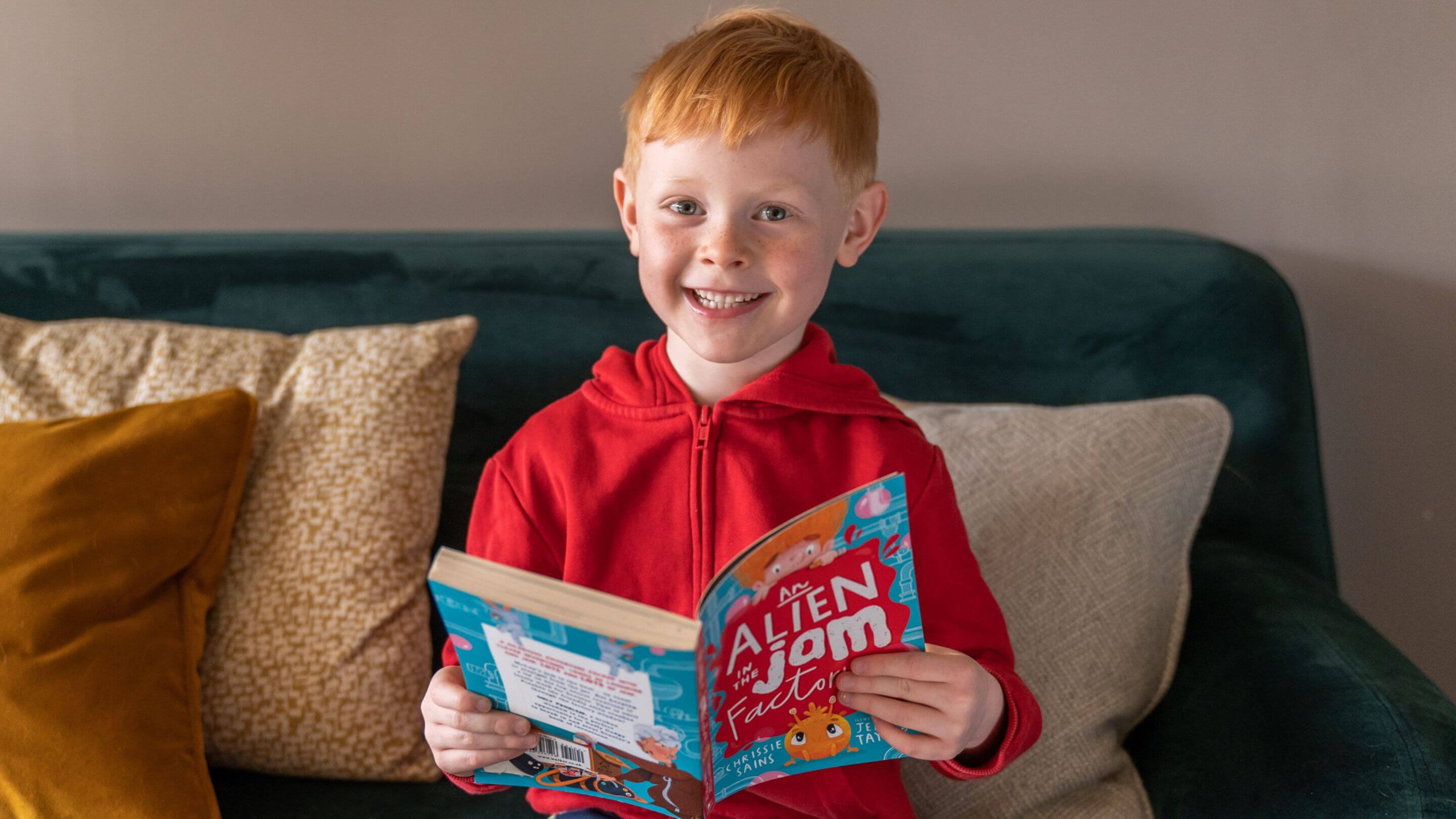 Smiling boy in a red top reading a chapter book from a Parrot Street subscription box