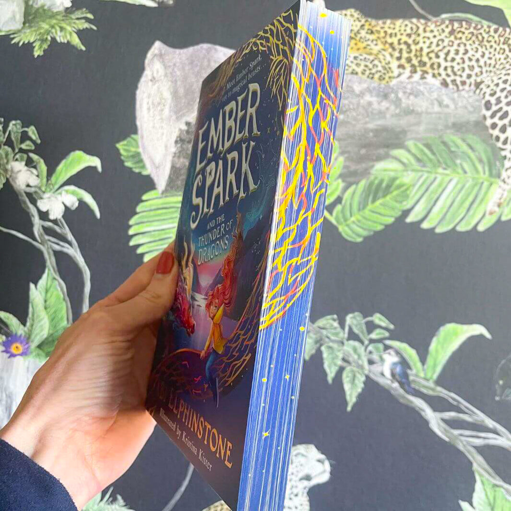 Hand holding a copy of Ember Spark and the Thunder of Dragons by Abi Elphinstone and showing the independent bookshop exclusive sprayed-edge