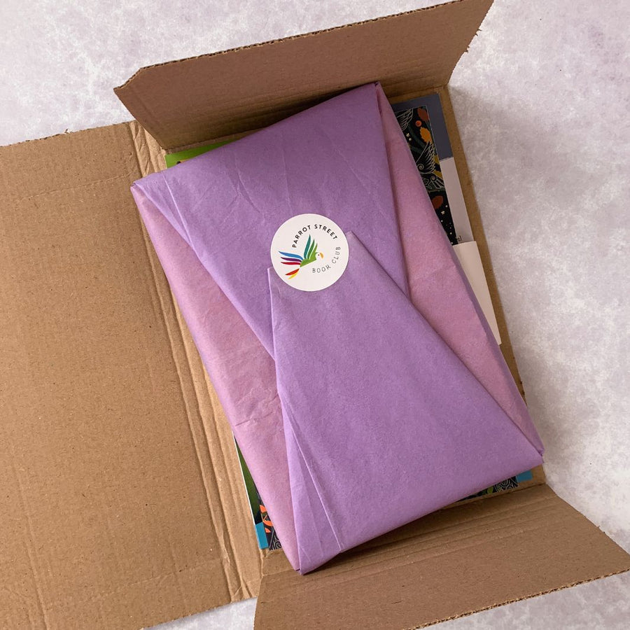 Single chapter book wrapped in purple tissue paper, resting inside a Cockatoo book subscription box.