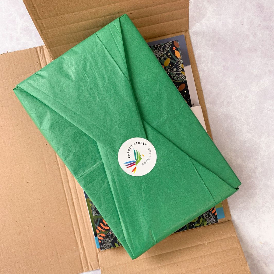Chapter book wrapped in tissue paper, resting inside a Macaw monthly subscription box