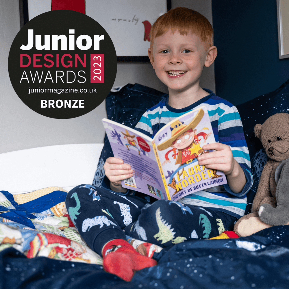 Smiling boy reading a chapter book in bed. Junior Design Awards winners logo is overlaid.