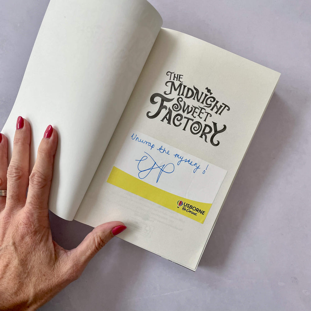 Open book with 'The Midnight Sweet Factory' title, signed bookplate and a hand holding it.