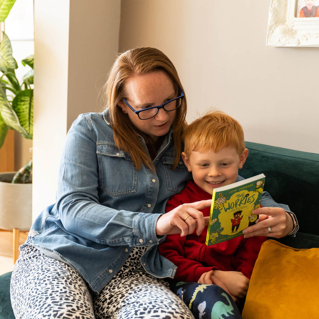 A mother and son sat on a sofa looking at a chapter book together