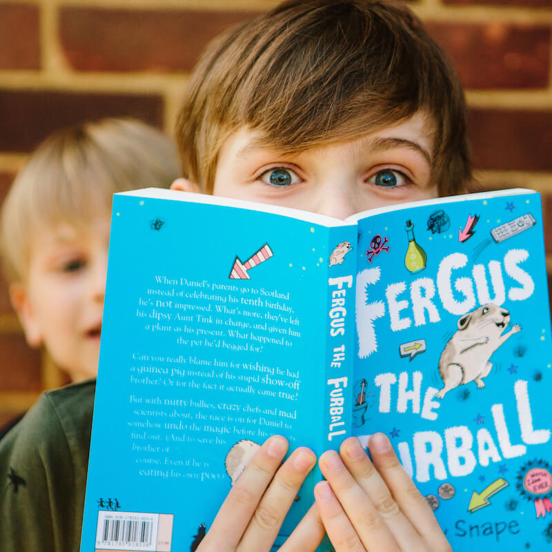 Child and sibling popping out from behind an open chapter book they're holding