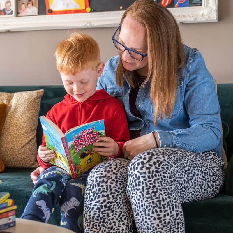 Mother and son sat together on a sofa reading a chapter book, part of a Parrot Street Book Club subscription box