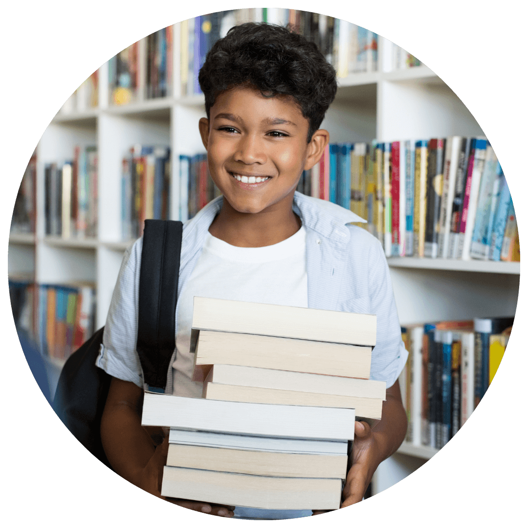 Smiling boy with a stack of books in a library